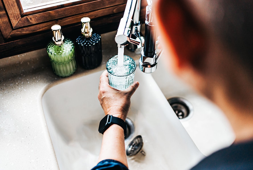 A glass being filled at a sink.